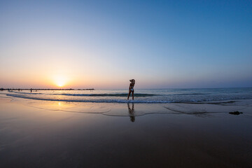 Fototapeta premium silhouette of a woman walking along the seashore. Spiritual Peace Meditation. A happy girl walks along the seashore against the backdrop of sunset.