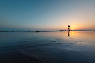 Fototapeta premium silhouette of a woman walking along the seashore. Spiritual Peace Meditation. A happy girl walks along the seashore against the backdrop of sunset.