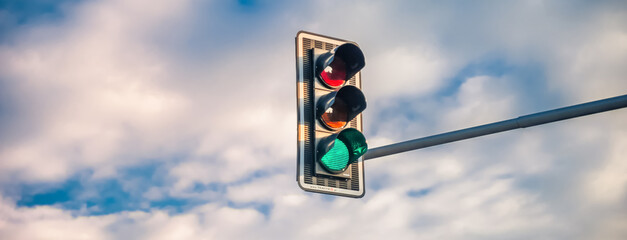 A traffic light with a green light on a background of a blue sky with white clouds. Banner - obrazy, fototapety, plakaty