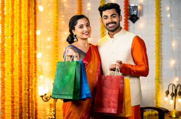 Happy young indian couple with shopping bags in hand looking camera - concept of festival offers,...