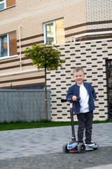 Child on a scooter on the yard. A little boy rides a scooter on a sunny day. Active sports for toddler.