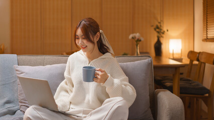 Fototapeta na wymiar Nightlife concept, Young woman drinks chocolate hot and watching movie on laptop in winter evening