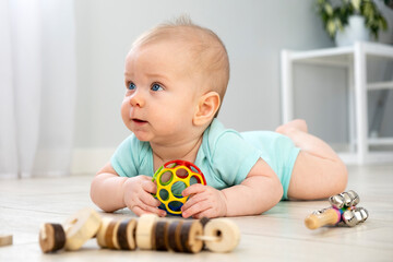 Cute little baby six months old in blue color bodysuit crawling on floor at home with light background and play wooden toys. Infant leisure at home.
