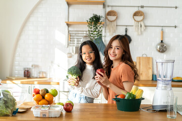 Portrait of enjoy happy love asian family mother and little asian girl daughter child having fun help cooking food healthy eat together with fresh vegetable salad and ingredient in kitchen