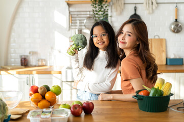 Portrait of enjoy happy love asian family mother and little asian girl daughter child having fun help cooking food healthy eat together with fresh vegetable salad and ingredient in kitchen