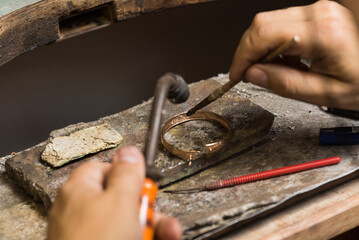 Close-up of the hands of a jeweler making repairs to a gold bracelet.