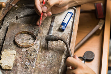 Close-up of the hands of a jeweler making repairs to a gold bracelet.