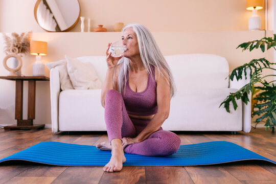 Woman drinking water sitting on yoga mat at home