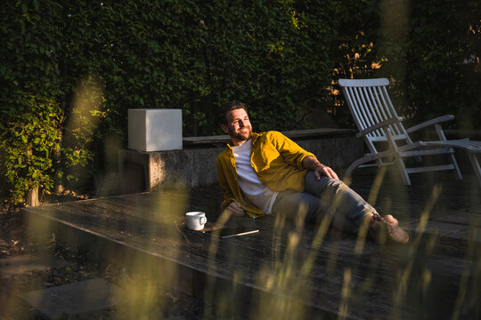 Happy Man With Coffee Cup And Tablet PC Relaxing On Porch