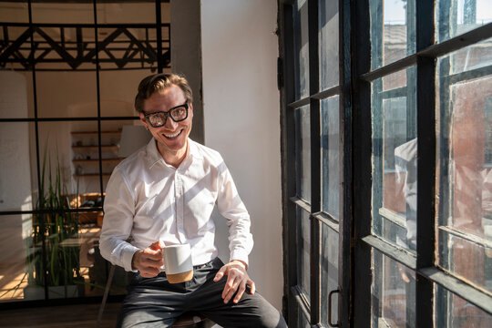 Happy mature businessman sitting with coffee cup by window