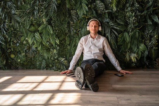 Mature businessman sitting on floor and listening to music - Powered by Adobe