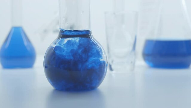 Blue liquid substance dissolve in a  glass flask. Concept for advertising perfume and cosmetic products. Mixing blue ink with water in a large laboratory glass test tube. 