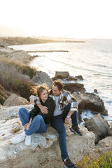 Portrait of a middle-aged couple sitting on a rock at the beach in Cyprus. They are wearing casual clothes