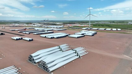 Wind turbine blades ready for shipping and installation. Manufacturing company of windmill parts. Aerial establishing shot with wind energy turbine in background.