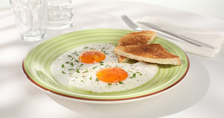 fried eggs with toast on a green plate. close-up. angle view. camera tracking. white background. traditional breakfast. sunny day.
