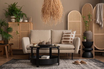 Warm and cozy living room interior with beige sofa, black round coffee table, boho lamp, rattan...