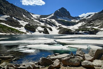 Fototapeta na wymiar picturesque blue lake with ice floes and mount toll on a sunny summer day from the lake shoreline in the indian peaks wilderness area, near nederland, colorado 