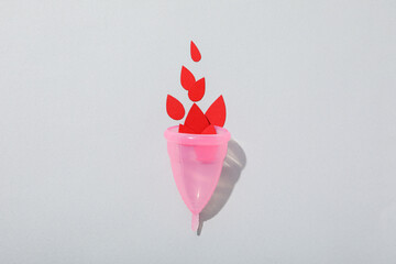 Pink menstrual cup with red drops in the middle, on a gray background