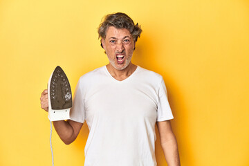 Man with iron in hand on a yellow background screaming very angry and aggressive.