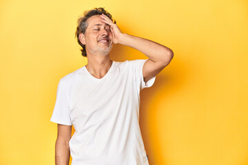 Middle-aged man posing on a yellow backdrop laughing happy, carefree, natural emotion.