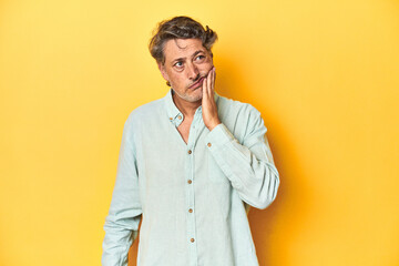 Middle-aged man posing on a yellow backdrop having a strong teeth pain, molar ache.