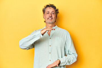 Middle-aged man posing on a yellow backdrop holding something with both hands, product presentation.