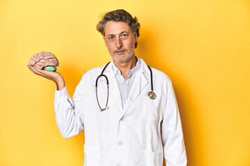 Middle-aged doctor holding a brain model, symbolizing neurology and knowledge.