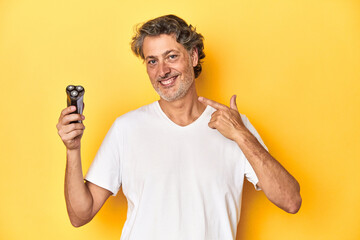 Man in the midst of a shaving routine with an electric razor on a yellow backdrop.