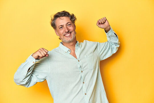 Middle-aged man posing on a yellow backdrop celebrating a special day, jumps and raise arms with energy. - Powered by Adobe