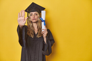 Young caucasian woman wearing a graduation robe holding a diploma Ystanding with outstretched hand...