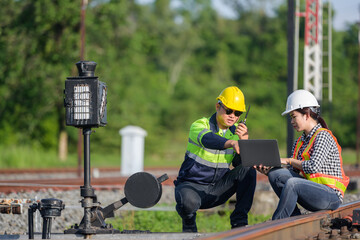 Asian railway worker or railway engineer maintaining railway track using laptop computer checking railway switch construction process and checking work in railway station.