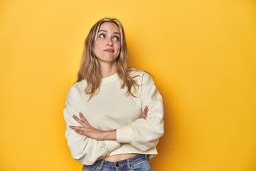 Young blonde Caucasian woman in a white sweatshirt on a yellow studio background, dreaming of...