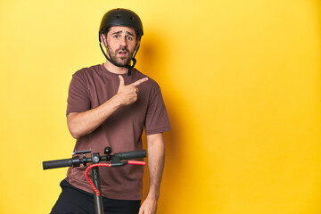 Fototapeta na wymiar Man with electric scooter and helmet, yellow studio pointing to the side