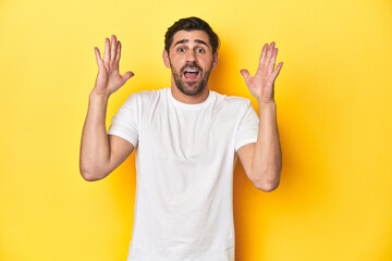 Caucasian man in white t-shirt on yellow studio background celebrating a victory or success, he is surprised and shocked.