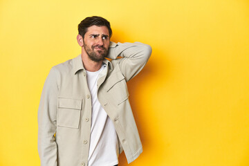 Caucasian man in grey shirt, studio shot on yellow touching back of head, thinking and making a choice.
