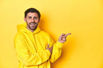 Man in yellow hoodie, monochrome studio backdrop smiling cheerfully pointing with forefinger away.