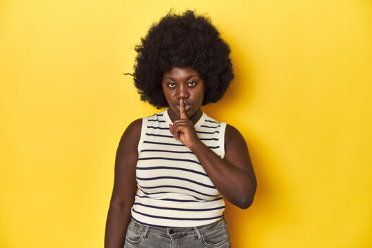 African-American woman with afro, studio yellow background keeping a secret or asking for silence.