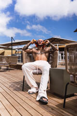 Fototapeta premium Chico joven tatuado y musculoso posando en terraza de chiringuito en vacaciones