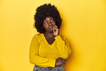 Fototapeta na wymiar African-American woman with afro, studio yellow background thinking and looking up, being reflective, contemplating, having a fantasy.