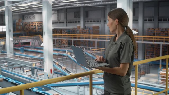 Logistics, Transportation Warehouse Facility: Female Supervisor Associate Uses Laptop. Center with Conveyor Loading Product Boxes for Online Shoppping Order Delivery to Customers. Static medium Shot