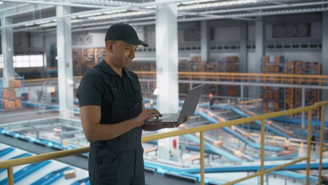 Logistics Transportation Warehouse Facility: Associate Worker Uses Laptop in Retail Distrubution Center, Controls Efficiency of Conveyor Loading Online Ordered Product Boxes for Delivery to Customers