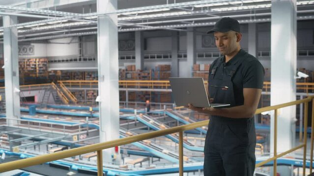 Logistics Transportation Warehouse Facility: Associate Worker Uses Laptop in Retail Distrubution Center, Controls Efficiency of Conveyor Loading Online Ordered Product Boxes for Delivery to Customers