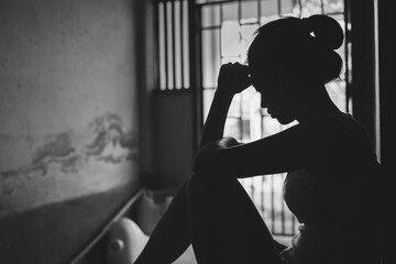 Silhouette of Depressed young woman near window at home, closeup in the dark room. domestic violence, violence against womenBlack and white photo.