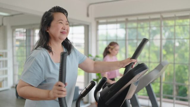 Happy elderly women talking with daughter while exercising on the machine in living room at home on weekend. Elderly lifestyle, Famity activity concept