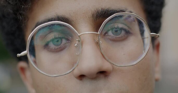 Close-up slow motion portrait of Middle Eastern man's face with eyeglasses looking at camera on outdoor background. Eyesight and youth concept.