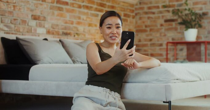 A woman shows an ultrasound image on a video call, talking on a mobile phone, sitting on the floor in a stylish home interior