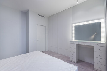 Bedroom with white interior decor. Double bed, wardrobe with hidden doors, dressing .table with mirror.