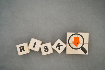 For risk management, business protection, strategy concept. Risk word on wooden cube and orange down arrow inside magnifying glass on blurred grunge grey background including copy space