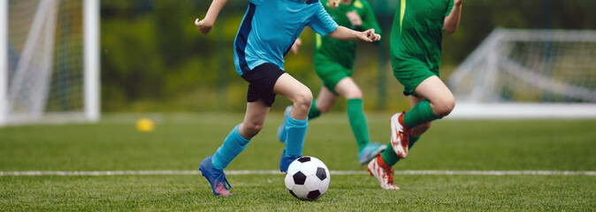 Junior level soccer competition between players running and kicking soccer. ball. Anonymous youth...