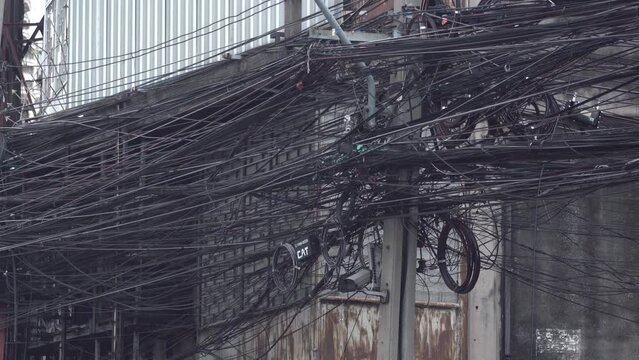 Messy power wires are tangled on the electrical pole, creating a chaotic arrangement of internet cables and powerlines in Thailand.